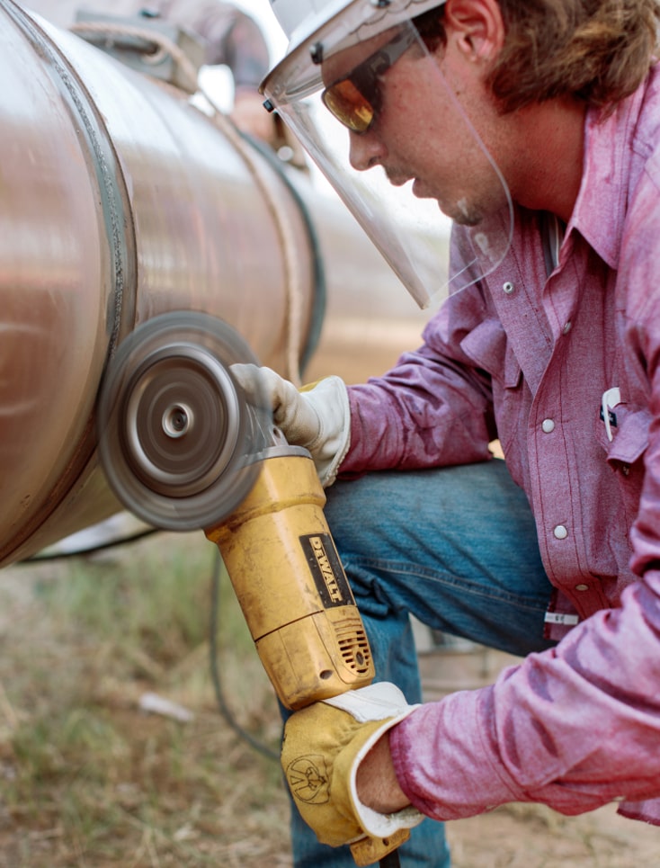 A photograph of a man close up, welding onto a large pipe.