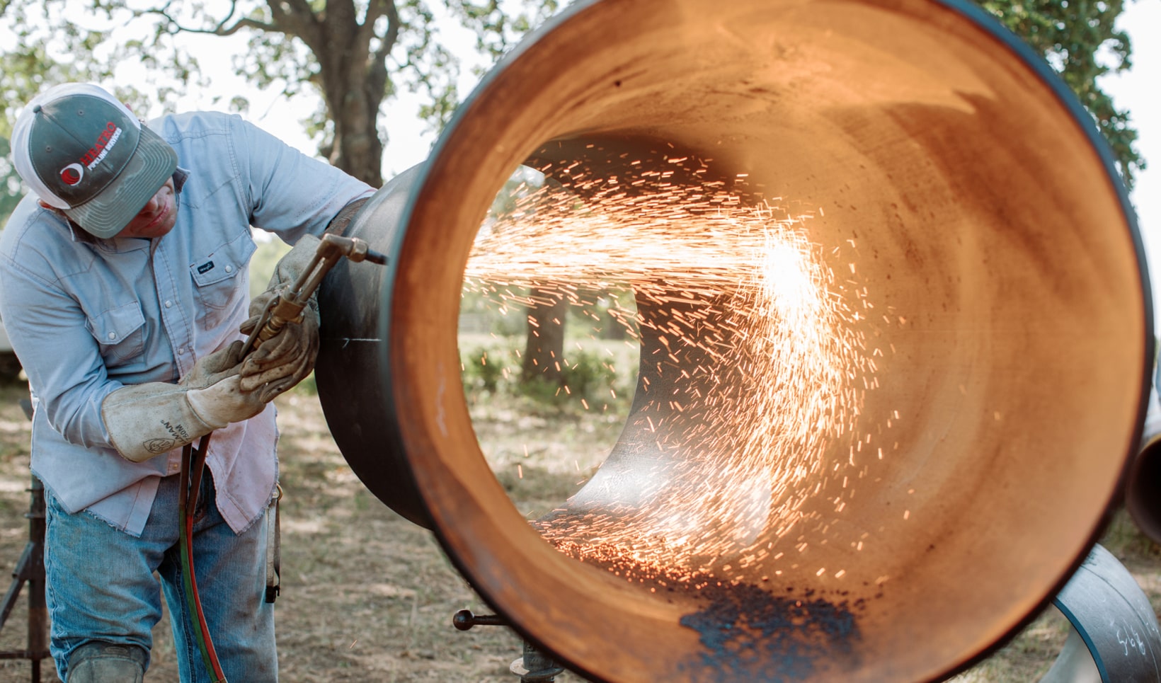 A photograph of a man welding on a pipe.