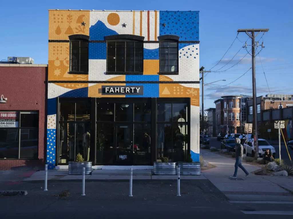 Storefront facade at sunset painted with an abstract geometric mural of mountains and sun shapes.